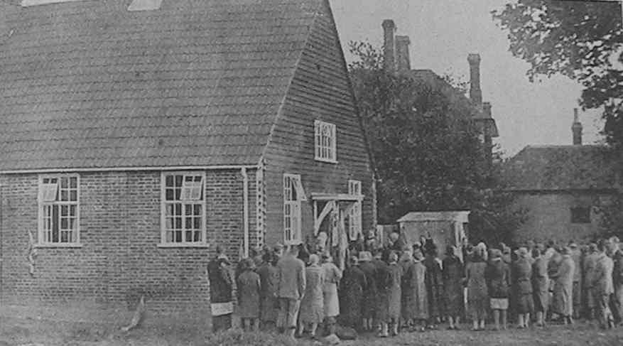 The crowd oustide the rear of the hall, with the village shop in the background